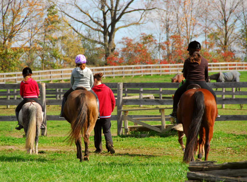 Three riders on horseback being lead by a volunteer