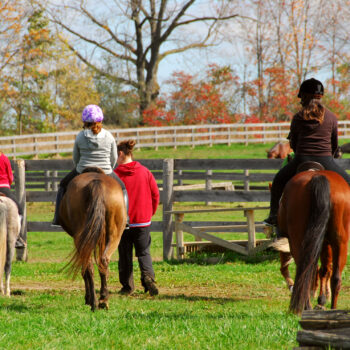 Three riders on horseback being lead by a volunteer